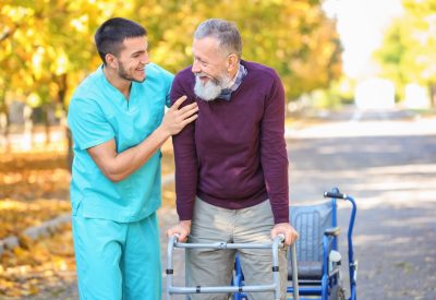 Young caregiver walking with senior man in park