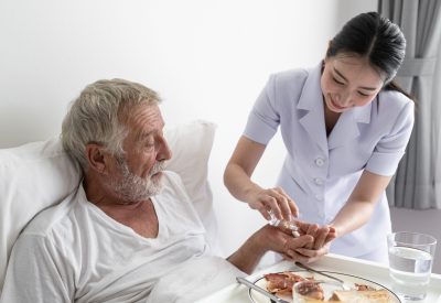 nurse give pill to senior man after breakfast and discussion on bed at nursing home