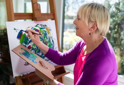 Happy elderly woman painting for fun at home